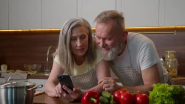 Kafkasyalı evli çift, aile bağı kuruyor olgun kadın, yemek tarifini cep telefonundan okuyor 50 'li yaşların yaşlı kocası, internetten alışveriş siparişi verirken mutfakta akıllı telefondan konuşuyor.