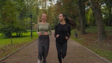 Mutlu kadınlar aktif, formda, beyaz kadınlar parkta birlikte koşuyor, gülümseyen iki kadın sporcu, koşan kadınlar sağlıklı bir yaşam tarzı sabah koşusu yapıyorlar.