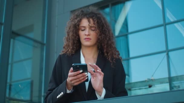 コーカサス州の女性女性女性労働者雇用主ビジネス起業家は ショックを受けたビジネスウーマンは 屋外の携帯電話の悪いニュースとのオフィスの故障問題の外の都市でスマートフォンを保持することを心配しました — ストック動画