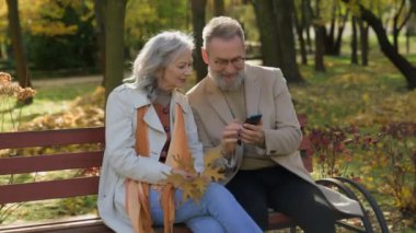 Güz parkında cep telefonu kullanan neşeli 60 'lı yaşlardaki kadın orta yaşlı koca iyi haberi kutluyor.