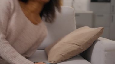 Afro-Amerikalı bir kadın kanepeye düşüp kanepede televizyon izlerken uzaktan kumandayla oturma odasında televizyon izlerken mutlu etnik kız konforu yayılıyor ve tembelce hafta sonu evde dinleniyor.