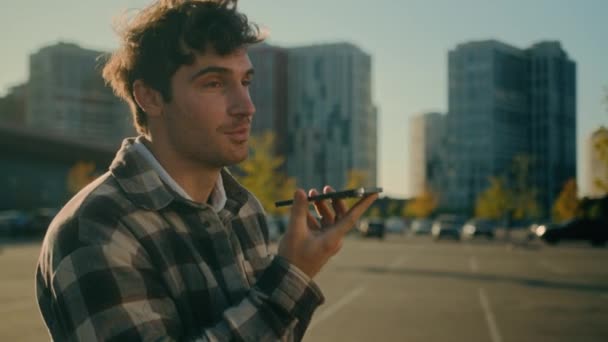 若いハンサムな男コーカサス男は スマートフォンで音声メッセージを記録する街を歩いています オンラインチャット屋外肯定的な笑顔ミレニアルは 携帯電話のスピーカーフォンに話すオーディオボイスメールを送信 — ストック動画