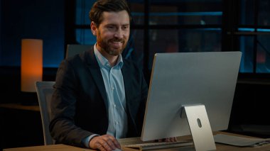 Orta yaşlı 40 'lı yaşlarda bir işadamı, bilgisayar işi için internet üzerinden gece vardiyasında çalışıyor. Beyaz, yetişkin, işveren, güler yüzlü, güler yüzlü, iyi bir sonuç.