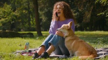 Mutlu Kafkasyalı genç kız evcil hayvan dostu kadın idareci neşeli bayan konuşan cep telefonu gülen sevimli köpek Welsh corgi köpek yavrusu şehir parkında yeşil orman yazında doğa