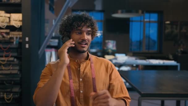 アラビアのインド人男性ファッションデザイナーテーラーアーティスト職人 ワークショップでクライアントを呼び出す トーク携帯電話笑顔の楽しい男性のクーリエ ファブリックストアでスマートフォンを話す手工芸服を設計 — ストック動画