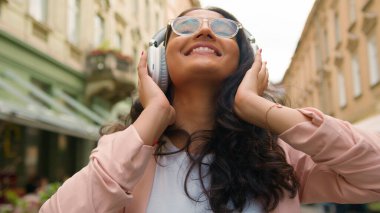 Neşeli, rahat, Hint Arap kökenli genç kız öğrenci bayan turist müzik listesi dinlemekten zevk alıyor. Müzik listesi uygulaması dans şarkıları, kablosuz kulaklıklar şehir sokaklarında ritim yaşam tarzı.