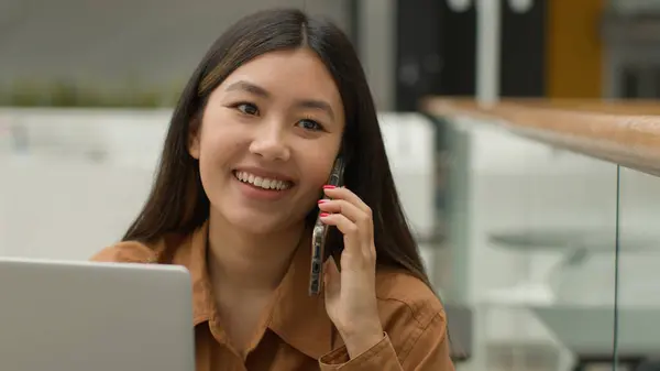 オフィスでラップトップでオンラインで働くアジアの女性ビジネス女性を笑顔中国の女子学生フリーランスの話携帯電話笑い興奮した女性の答えスマートフォン呼び出し屈託のない会話 — ストック写真