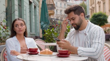 Kafkasyalı çift şehir kafeteryasında kahvaltı yapıyor. Meşgul erkek arkadaş cep telefonu kullanıyor. Üzgün kız arkadaşı görmezden geliyor.