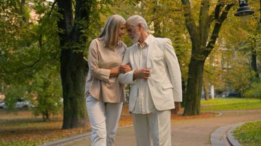 Mutlu, sağlıklı, yaşlı, yetişkin, Kafkasyalı büyükanne ve büyükbaba, şehir parkının dışında el ele yürüyen ve birlikte kahkahalar atan erkek aile çiftleriyle evli. Nostalji anıları emekliliği
