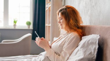 Mutlu gülümseyen güzel kız etkili blog yazarı Kafkasyalı kadın bağımlı zımbırtı gülümsemesi uyan cep telefonu uygulaması sosyal medya ağı sabah rahat yatağında akıllı telefon kaydırmalı yemek siparişi