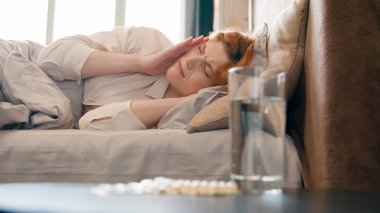 Bir bardak su ve ilaç. Masada ağrı kesici. Hasta, hasta, sağlıksız, baş ağrısı çeken, akşamdan kalma, migren ağrısı çeken baş ağrısı çeken bir kadın.