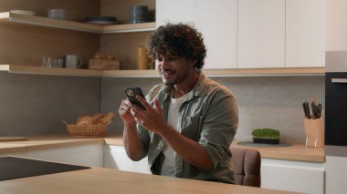 Hareket eden kamera zoom 'u, mesaj alan adamın Hintli mutlu Arap erkek haberlerini akıllı telefondan kazanmasına hayret etti. Mutfaktaki başarılı cep telefonu zaferini kutlayan heyecanlı adam