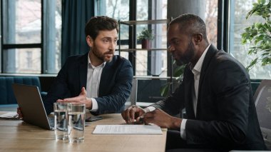 Çeşitli çok ırklı Afrikalı Amerikalı ve Kafkasyalı iş arkadaşları iş adamları finans ajanları ofis bilgisayarlarıyla başlatılan iş projelerini evrak evraklarıyla tartıştılar.