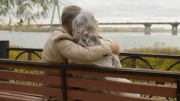 Back view old married couple romantic moment man embracing woman on bench in park happy family gray-haired intelligent male female love hugging cuddling relax together holidays outdoors nature city