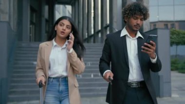 İki iş ortağı Arap iş kadını şehir havaalanında yürüyen cep telefonlarıyla konuşan Hintli işadamını arıyor bavul valizli akıllı telefonu araştırıyor.