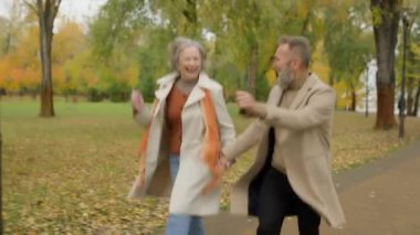 Mutlu son sınıf çifti, güz parkında zıplayarak dans ediyor evli çiftler açık havada komik, sağlıklı eşler iki yaşlı kadın emekli insanlar şehirde sokaklara atlıyor kaygısız bir tatil yapıyorlar.