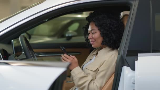 非洲女人笑着用智能手机在线聊天在新的现代豪华轿车里发短信快乐车主美国女买家用手机支付租车费用 — 图库视频影像