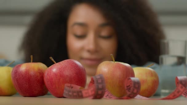 ハッピーヘルス微笑むアフリカ系アメリカ人女性 家庭用キッチンで女性 テーブルでの水測定テープのフルーツリンゴグラスを楽しんでいる 食事療法 健康的な栄養ダイエット スリム — ストック動画
