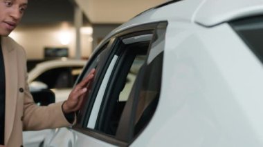 Afro-Amerikalı etnik adam gülümseyen müşteri galeride araba dükkanının içine bakıyor. Erkek işadamı, araba eleştirmeni, yeni lüks otomobil satın alma hayalleri kuruyor.
