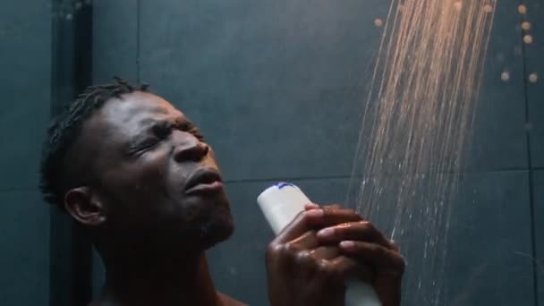 密切关注快乐快乐的黑人黑人男子赤身裸体在浴室里唱歌玩得很开心拿着瓶子洗发水每天唱洗发水皮肤卫生听音乐放松 — 图库视频影像