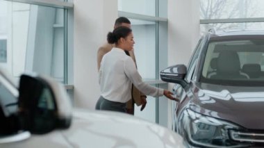 Afro-Amerikalı kadın satış danışmanı otomobil satıcısı. Müşteri alıcısına otomobili incelemesinde yardım et. Yeni bir geçiş kamyonu seç.