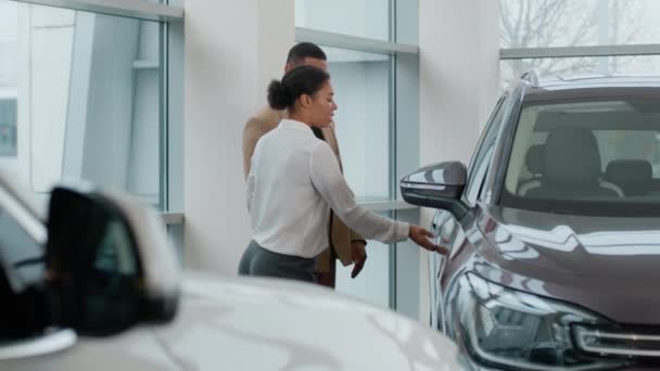 非洲裔美国女销售员女销售员汽车经销商帮助男人顾客买方检查汽车选择新的越野车现代豪华电动汽车在经销商陈列室 — 图库视频影像