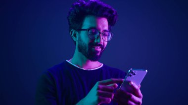 Arap erkek cep telefonuyla sohbet ediyor, akıllı telefonları tarıyor cep telefonuyla alışveriş siparişi veriyor Hintli adam Neon ultraviyole stüdyonun arka planında sosyal medya internet teknolojisi uygulaması kaydırıyor.