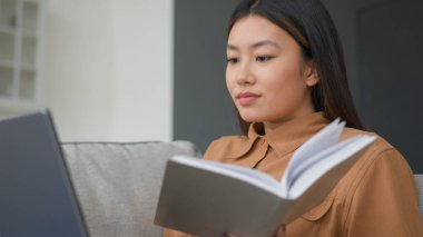 Asyalı iş kadını kanepesinde dizüstü bilgisayar kullanıyor evde bilgi edinme eğitimi alıyor iş planı yazıyor not defterine notlar yazıyor Koreli kız öğrenci izleme dersi internetten ödev yapıyor