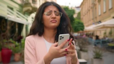 Sinirli Hintli Arap etnik kadın cep telefonu arızalı cep telefonu kullanmaktan rahatsız oluyor. Kötü uygulama Wi-Fi bağlantısı, şehir merkezindeki kafenin dışında kötü haber veriyordu.