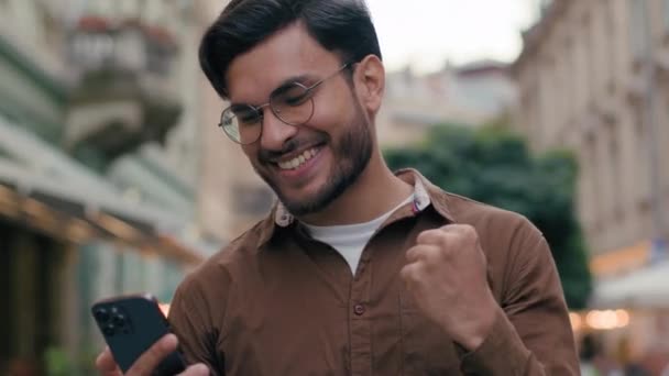 クローズアップ幸せな幸運な遺伝子 インド アラビアの民族男性 ビジネスマン 受賞者 携帯電話を指す 指の拳のジェスチャー 楽しむ オンライン ビジネス勝利宝くじ — ストック動画