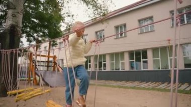 Avrupalı kız çocuk oyun parkında oynuyor, küçük kız öğrenci ip yolda yürüyor, dinlenme dersleri alıyor, eğitim dışında tırmanış dersleri alıyor ilkokul sportif aktif yaşam tarzı hareketi kuvveti.