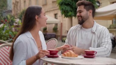Genç Avrupalı çift birlikte kahvaltı yapıyor mutlu erkek kadın gülümsüyor tatlı öpücükler el ele tutuşuyor aşıklar şehri kafeterya restoranının dışında romantik balayı şefkatli bir evlilikle çıkıyor.