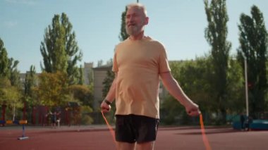 Yaşlı beyaz adam ip atlama sporcusu gülümseyen stadyum şehri spor dışında fiziksel aktivite yaşlı sporcu antrenmanı sağlıklı sağlık hizmetleri güçlü kas gücü egzersizi.