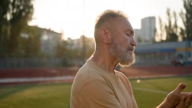 Kendinden emin Avrupalı yaşlı sporcu sıcak elleriyle ovuşturuyor antrenman hazırlıyor ısınma egzersizleri yapıyor eski stadyum açık havada sağlıklı vücut bakımı fiziksel aktivitesi