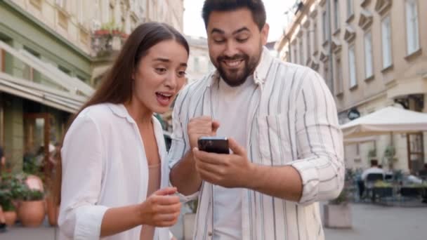 コーカサスカップル幸せな女性男性は 携帯電話ハイファイブ除外成功の感情を達成した携帯電話の携帯電話を使用して喜び一緒に勝利ラッキーな表現に喜んで喜んでいます 外の勝利都市を喜びます — ストック動画