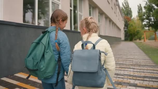 回头看两个女学生牵着手走在街头的城市里跳跳着学习的小女孩和好朋友聊着好玩的姐姐在一起学习教育的小学生 — 图库视频影像