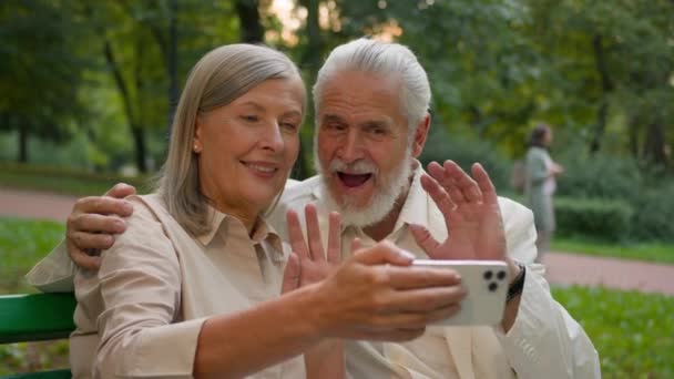 スマートフォンアウトドアシティパークを使用してリラックスして話す白人中年老いた家族のカップルを微笑むポートレートを閉じます 幸せな祖父母オンラインビデオ通話妻夫のコミュニケーション接続 — ストック動画