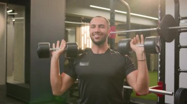 Mutlu gülümseyen Afrikalı Amerikalı adam spor salonundaki dambılları kaldırıyor spor spor spor spor spor spor spor antrenörü vücut geliştirme sporu sporcusu vücut geliştirme sporcusu ağırlık egzersizi yapıyor vücut geliştirme egzersizi yapıyor ağırlık egzersizi yapıyor kas antrenmanı yapıyor.