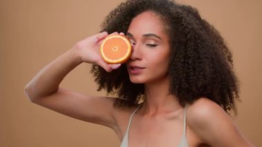 Etnik model kız portresi stüdyosu arka planı Afro-Amerikan kadın mükemmel cilt sağIıklı saç lüleleri turuncu meyve teninin yarısını tutan doğal organik ürün vegan formülü narenciye yağı kozmetik ürünleri