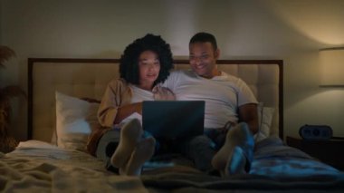 Bilgisayar bağımlısı çift mutlu aile kız arkadaşı ve erkek arkadaş birlikte dizüstü bilgisayar kullanan Afro-Amerikalı erkek ve kadın alışveriş merkezi alışverişini seçip yatak odasında tartışırlar.