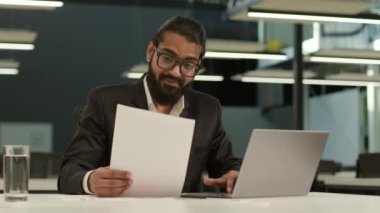 Odaklanmış Hintli işadamı Arabistanlı girişimci Hindu iş adamı erkek yönetici işvereni ofis daktilo bilgisayarı araştırma verilerini kağıt evraklarında kontrol ediyor.