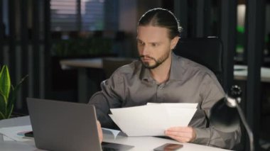 Konsantre iş adamı araştırması sonucu şirket yazışmalarını analiz eder. Erkek adam evraklardaki verileri kontrol eder. Ve laptop işadamı karanlık ofis işleri zamanında bilgisayar evrak işleriyle meşgul olur.