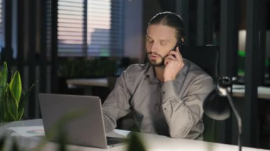 Gece geç saatlerde gülümseyen Kafkasyalı işadamı. Bilgisayarda çalışan, bilgisayarla konuşan, cep telefonuyla konuşan, akıllı telefon görüşmeleri yapan, müşteri temsilcisine danışın.
