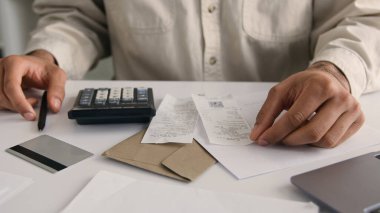 Tanınmayan bir erkek iş adamı hesap makinesi ve dizüstü bilgisayar kullanıyor. Gelir hesabı yapıyor. Faturaları sayıyor.