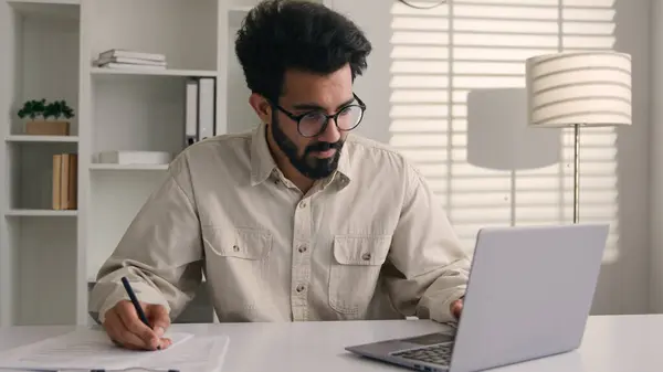 焦点を当てた男性アラビアのインドのエスニックビジネスマン男性の従業員マネージャーは ノートを書く ビジネスタスク データ書類署名文書 オフィスのラップトップコンピュータで作業する予算を数える紙に書きます — ストック写真