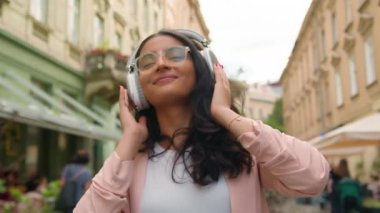 Neşeli, rahat, Hint Arap kökenli genç kız öğrenci bayan turist müzik listesi dinlemekten zevk alıyor. Müzik listesi uygulaması dans şarkıları, kablosuz kulaklıklar şehir sokaklarında ritim yaşam tarzı.