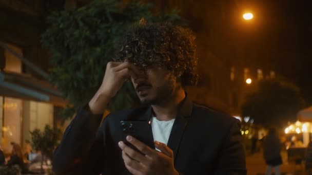 インドのアラビアのラティーノ 携帯電話を保持している男性は怒っている怒っている狂気の男性の携帯電話のユーザー テクノロジー都市を夜外で否定的なトラブル スパムの激しい通知が失われた — ストック動画