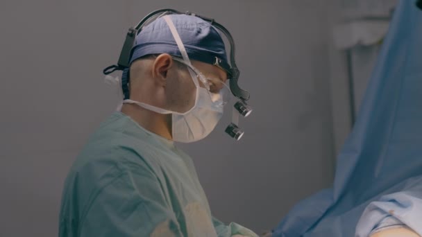 男性医師 外科医 神経外科医 医療マスクの実践医 病院の医療で顕微鏡を用いた手術室疾患手術で手術を行います — ストック動画
