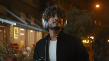 Hintli Arap Latin Amerikalı adam şehir caddesinde yürüyor. Cep telefonu çalıyor. Müzik dinliyor, kahve içiyor.