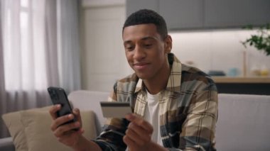 Gülümseyen Afrikalı Amerikalı erkek alıcı uzak müşteri kullanıcı internet üzerinden ödeme bankası uzaktan satın almak cep telefonu alışverişi mal teslimatı tasasız erkek etnik adam ev satın